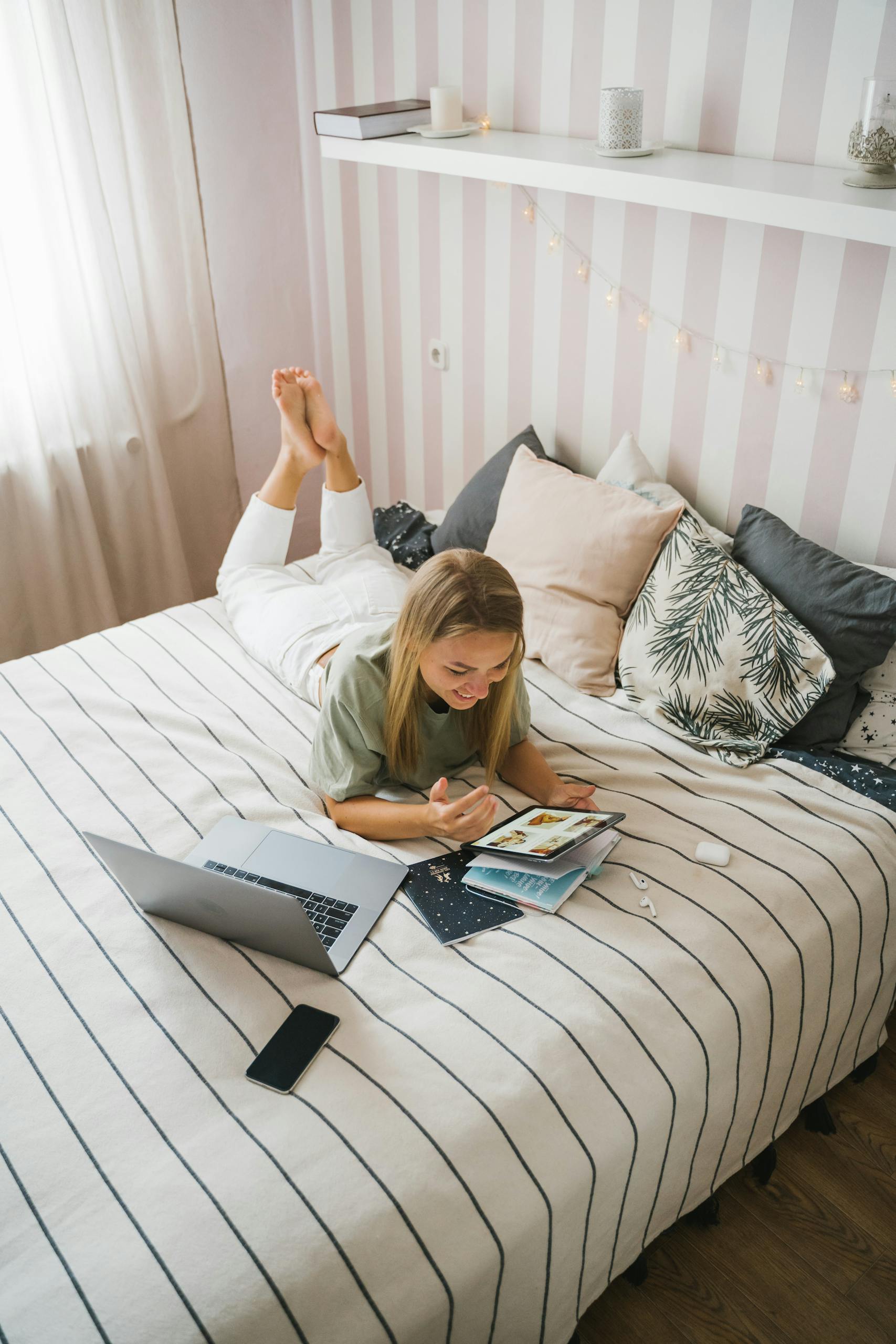 A woman comfortably working from bed with a laptop and notebook, in a cozy home office setup.